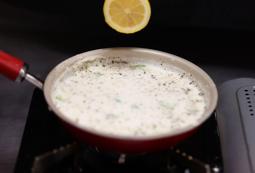 Hand squeezing lemon over skillet