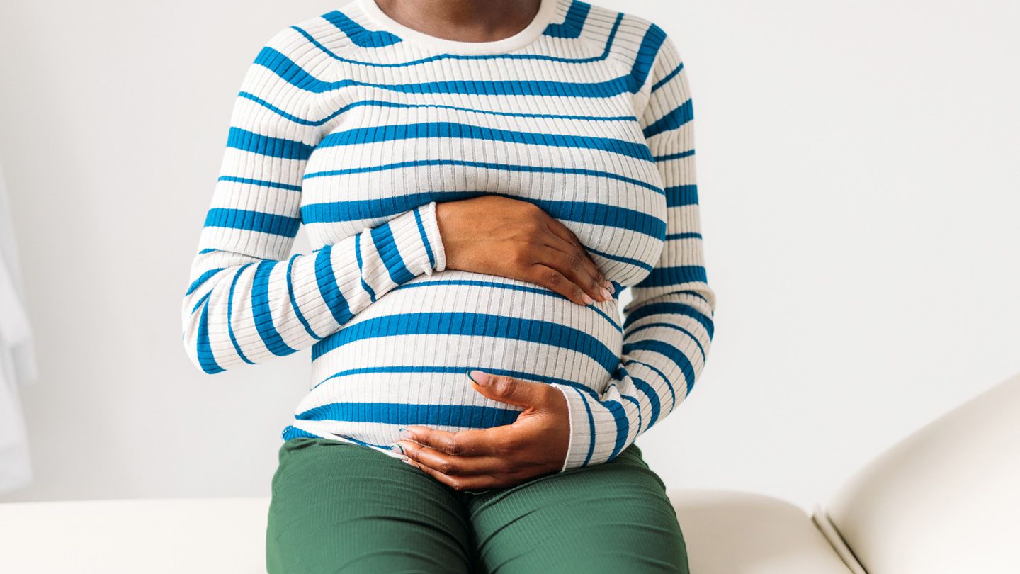 Pregnant woman clutches belly near couch