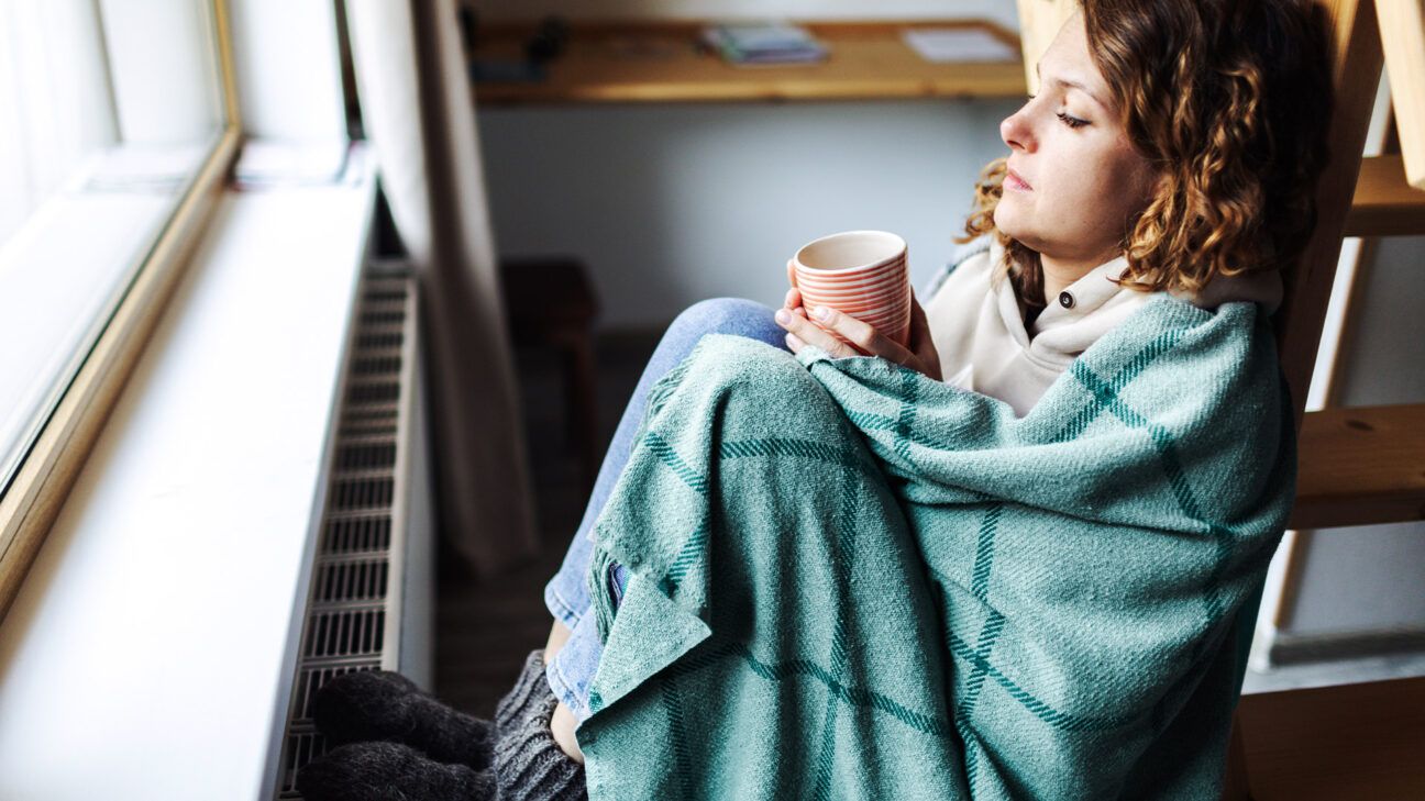 Sick woman wrapped in blanket drinking tea