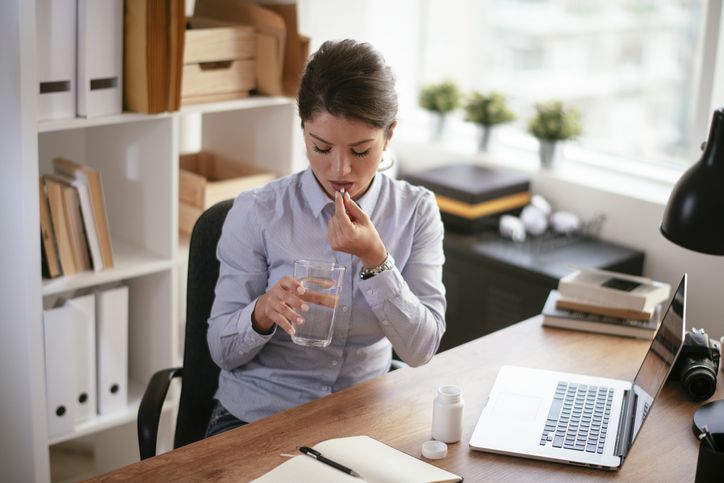 woman taking pill at office desk