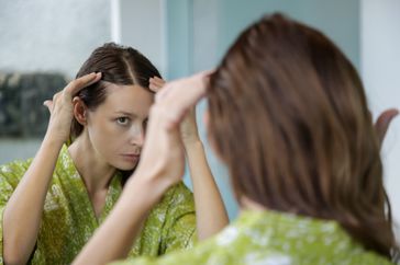 Woman inspecting hair in bathroom mirror