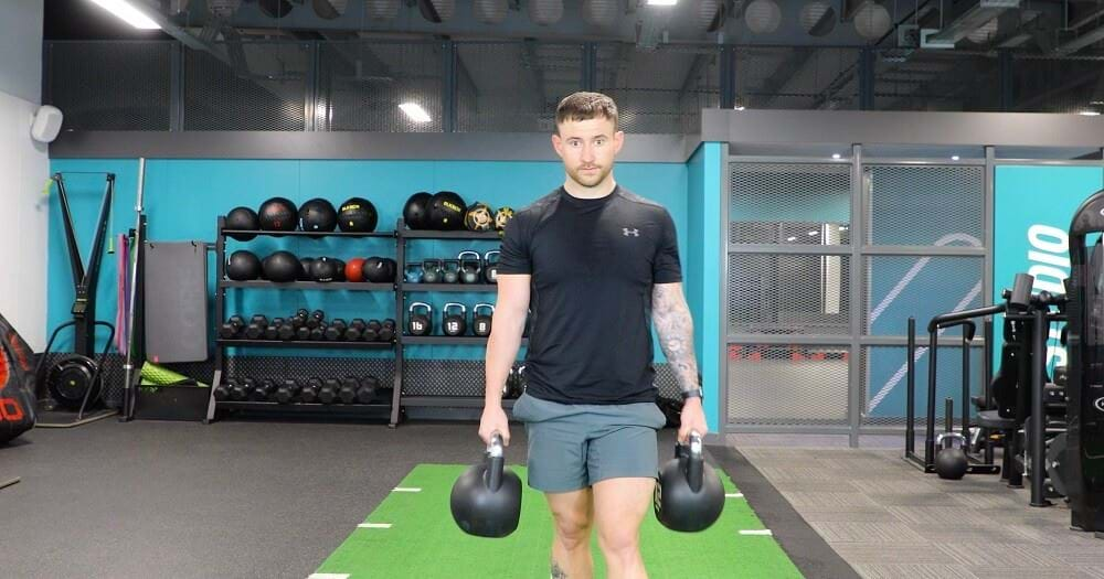 Man doing farmers walk with kettlebells